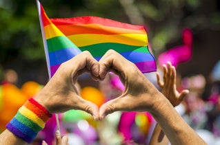 hand doing heart shape with rainbow flags