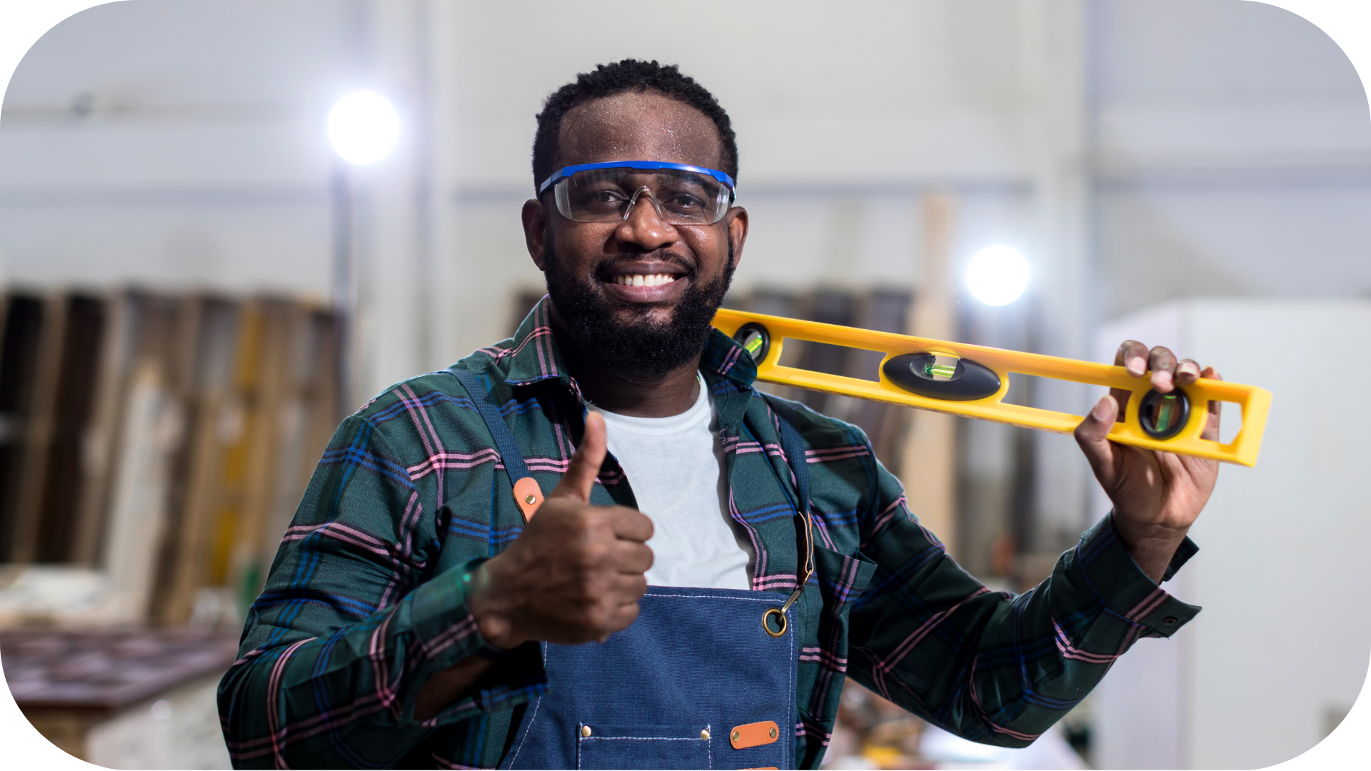 A man working in a shop, holding a level and giving a thumbs up